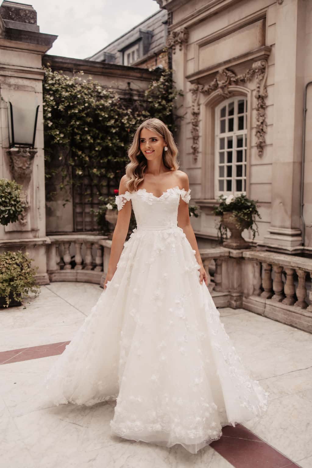 Bridal Designer Suzanne Neville Debussy Overskirt wedding gown has a corseted cupped bodice with off the shoulder floral straps and Debussy floral tulle overskirt. Find your wedding dress at Your Dream Bridal in near Boston.